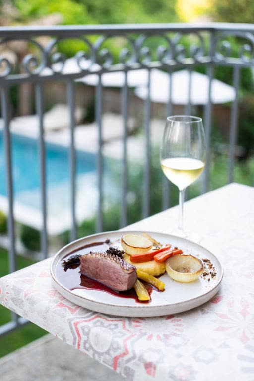 Assiette bistronomique et verre de vin blanc sur la terrasse avec vue sur la piscine